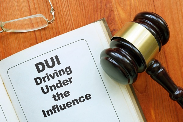 A wooden judge's gavel resting on an open law book that displays the text "DUI Driving Under the Influence" alongside a pair of eyeglasses on a wooden desk.