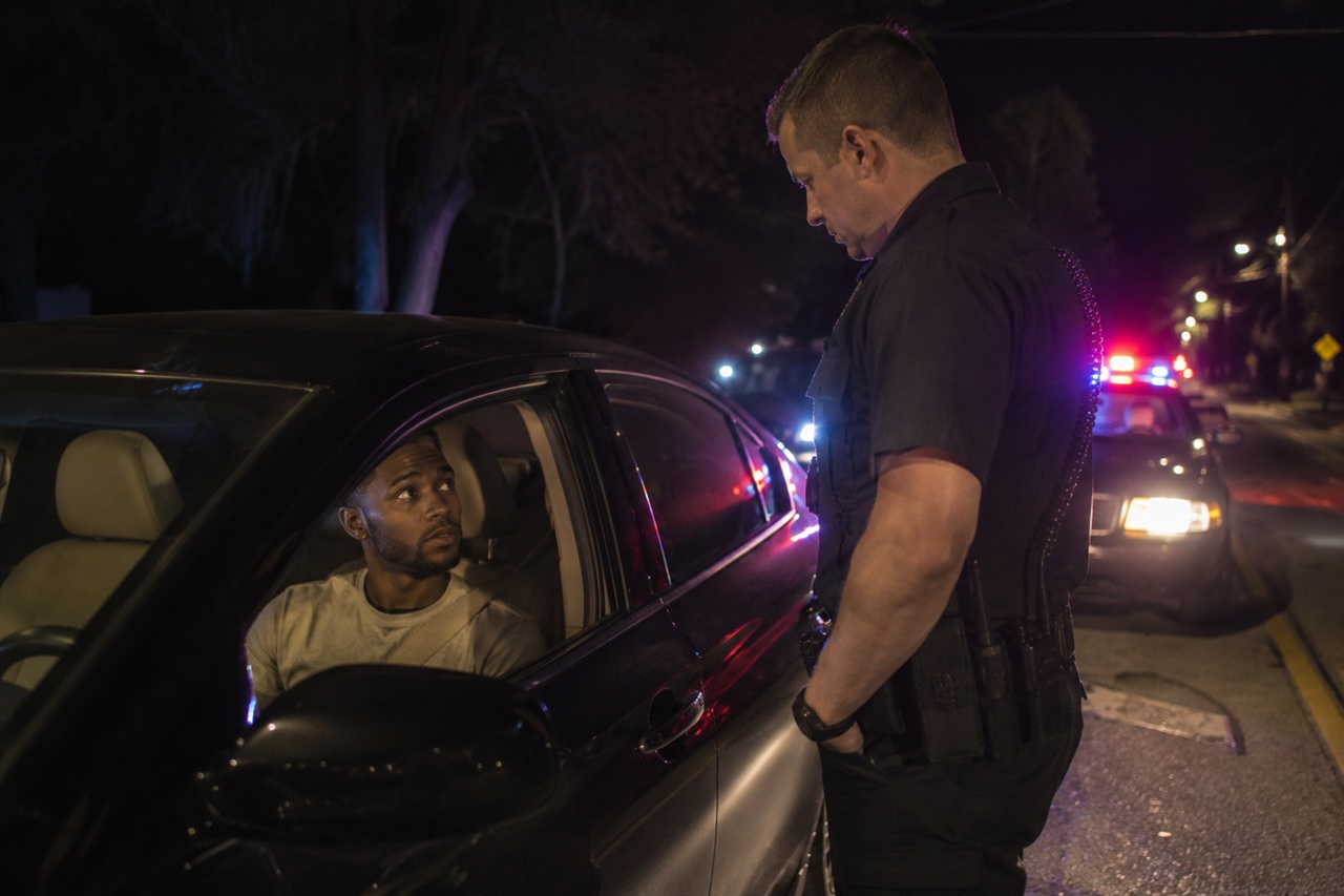 A police officer speaking to a driver during a nighttime traffic stop with patrol car lights visible in the background, illustrating a scenario where a motorist in South Carolina may face charges for either Driving Under the Influence (DUI) or Driving with an Unlawful Alcohol Concentration (DUAC).