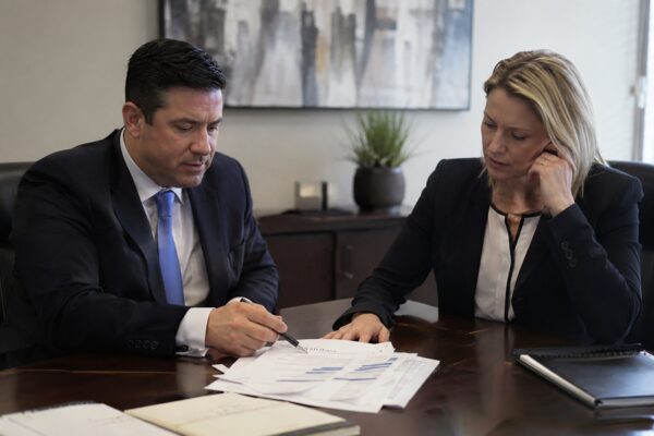 A defense attorney and a client in professional attire sit together at a conference table reviewing financial documents with charts, depicting a South Carolina criminal defense consultation for a client facing embezzlement or theft charges.